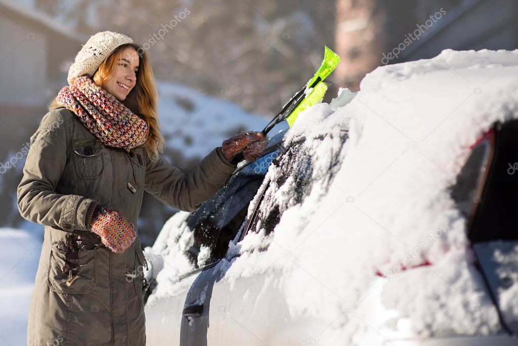 Woman remove snow from car with snow brush.