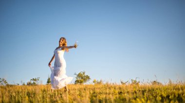 Gün batımında çayır üzerinde genç romantik kadın. Beyaz elbiseli kız açık havada sahiptir. Ilık ışık