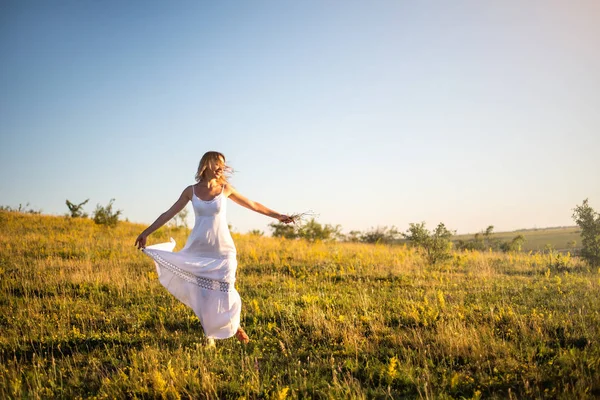 Gün batımında çayır üzerinde genç romantik kadın. Beyaz elbiseli kız açık havada sahiptir. Ilık ışık