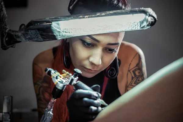 Tattoo master at work. Woman tattoo master in process of creation tattoo under the lamp light.