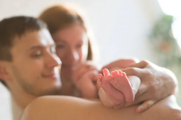 L'attenzione sulle gambe del neonato. Caucasico sorridente padre e madre abbracciando teneramente adorabile bambino appena nato. Felice concetto di famiglia.Deadpan grezzo foto nofilter — Foto Stock