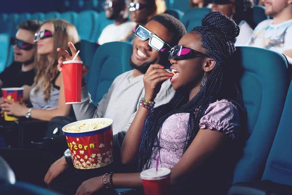 Un par de africanos comiendo palomitas de maíz, bebiendo cola en el cine . — Foto de Stock