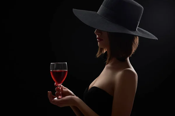 Elegant mysterious woman in a hat holding a glass of red wine on Stock Photo