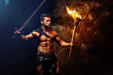 Fearless young muscular warrior with a torch in the dark clipart