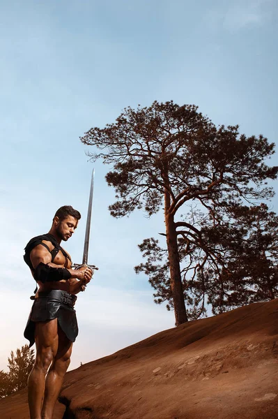 Young muscular warrior with a sword at the mountains — Stock Photo, Image