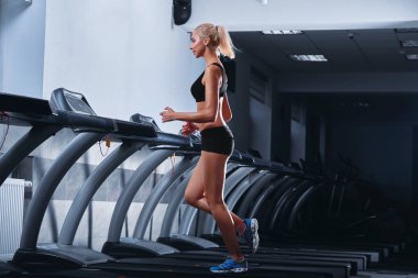 Genç güzel atletik kadın spor salonunda bir koşu bandı üzerinde çalışan