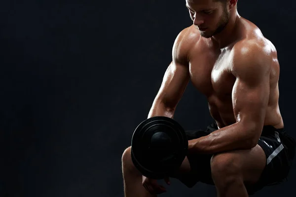 Muscular young man lifting weights on black background — Stock Photo, Image