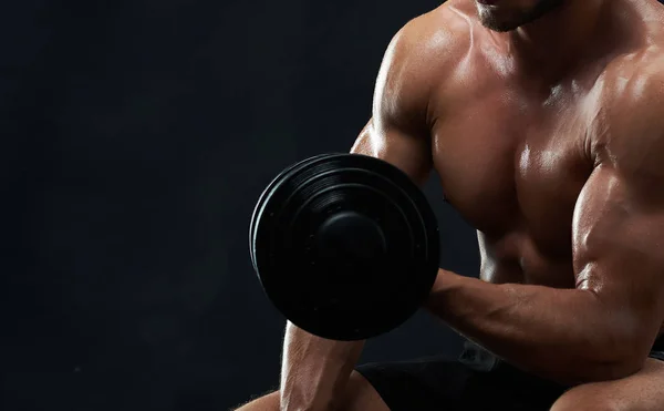 Muscular jovem levantando pesos no fundo preto — Fotografia de Stock