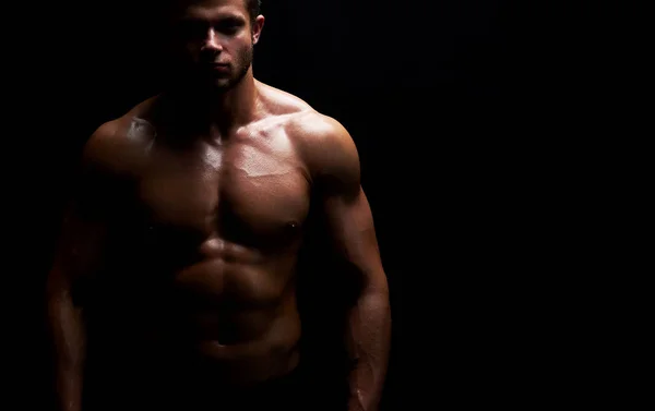 Junger muskulöser Sportler posiert hemdlos auf schwarzem Hintergrund — Stockfoto