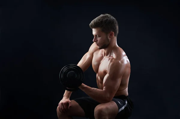 М'язистий молодий чоловік піднімає ваги на чорному тлі — стокове фото