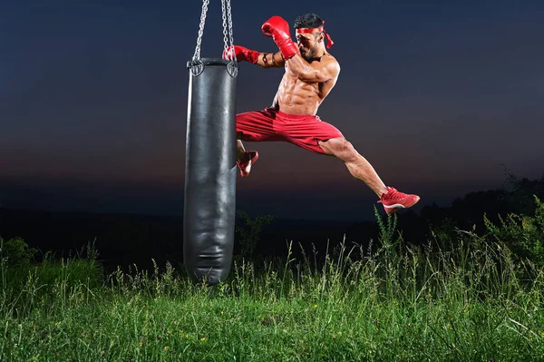Ung snygg manliga boxare tränar på en slagsäck utomhus — Stockfoto