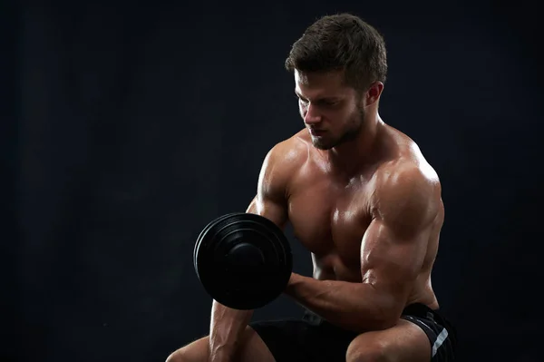 Muskulöser junger Mann stemmt Gewichte auf schwarzem Hintergrund — Stockfoto