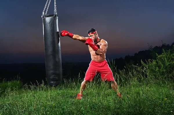Joven guapo boxeador masculino practicando en un saco de boxeo al aire libre — Foto de Stock