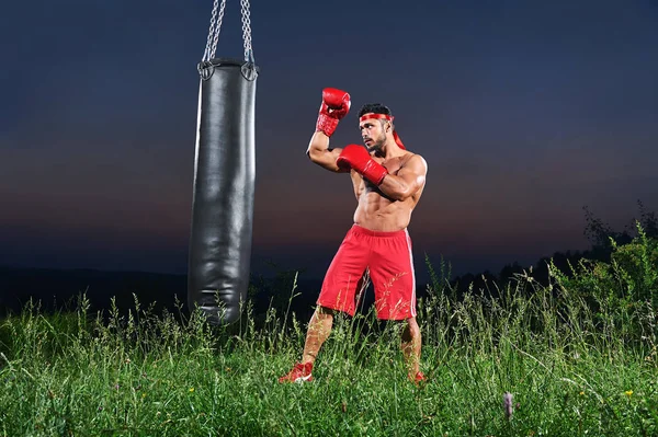 Mladý pohledný muž boxer cvičení na boxovací pytel Outdoor — Stock fotografie