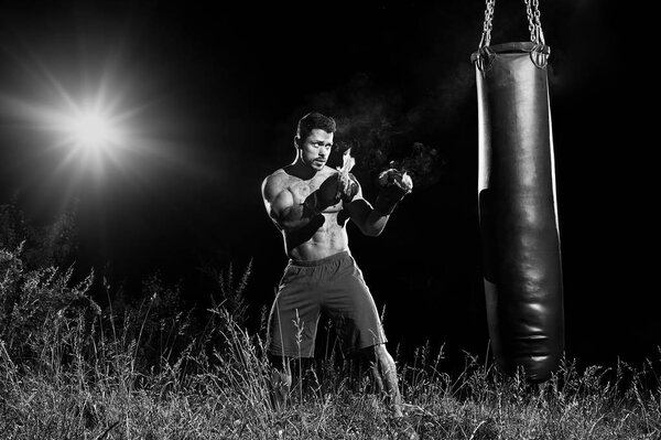 Professional boxer punching sandbag outdoors with his boxing glo