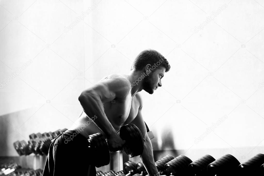 Monochrome shot of a ripped shirtless man exercising with dumbbe