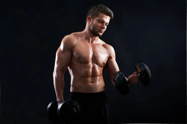 Musculoso joven levantando pesas sobre fondo negro — Foto de Stock