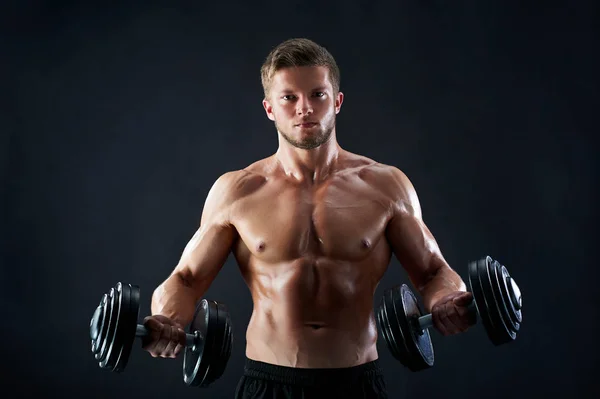 Muskulös ung man lyfta vikter på svart bakgrund — Stockfoto