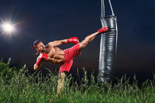 Молодий красивий чоловічий боксер практикує на ударній сумці на відкритому повітрі — стокове фото