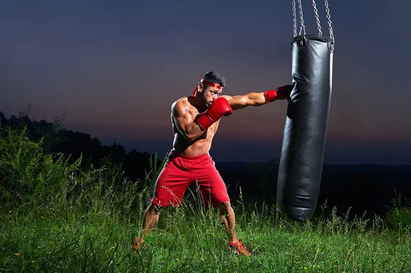 Joven guapo boxeador masculino practicando en un saco de boxeo al aire libre — Foto de Stock