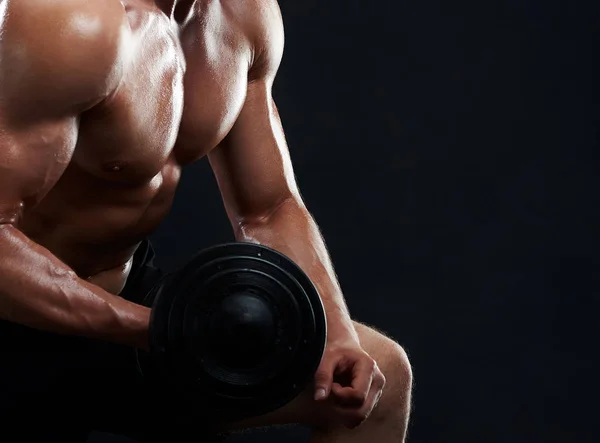 Musculoso joven levantando pesas sobre fondo negro —  Fotos de Stock