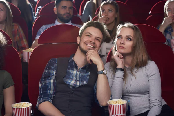 Serious woman and smiling man watching movie at modern cinema.