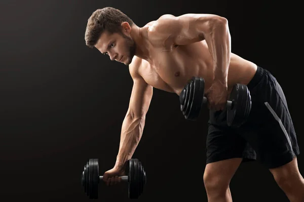 Muscular young man exercising with dumbbells — Stock Photo, Image