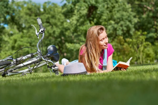Mujer joven leyendo un libro después de andar en bicicleta en el parque local — Foto de Stock
