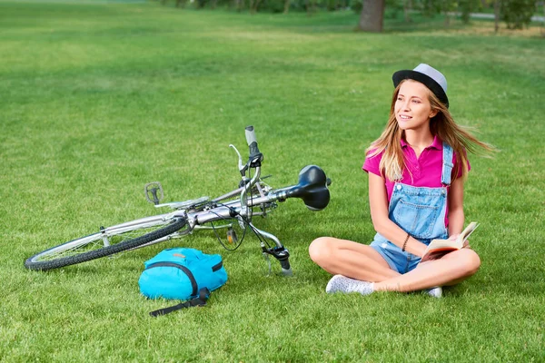 Junge Frau liest nach Fahrradtour im Stadtpark ein Buch — Stockfoto