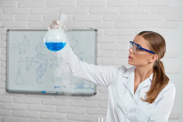 Молодая женщина анализирует голубую химическую жидкость — стоковое фото