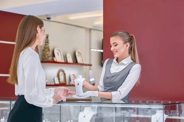 Блондинка-працівник у сірій формі, що показує намисто для жіночого клієнта в ювелірному магазині . — стокове фото