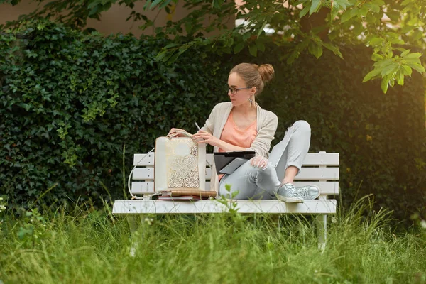 Egy fiatal lány ül a fehér padon a parkban — Stock Fotó