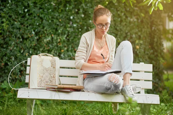 Young student writes on the park s bench