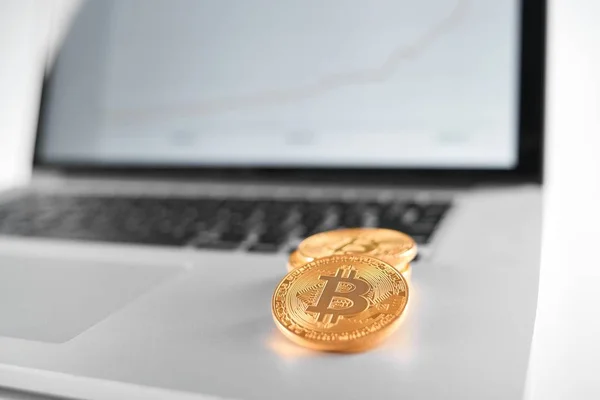 Sharp focus on golden bitcoins placed on silver laptop with blurred financial chart on its screen — Stock Photo, Image