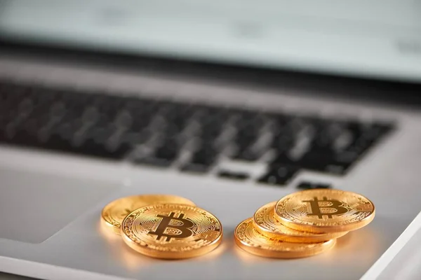 Sharp focus on golden bitcoins placed on silver laptop with blurred financial chart on its screen. — Stock Photo, Image
