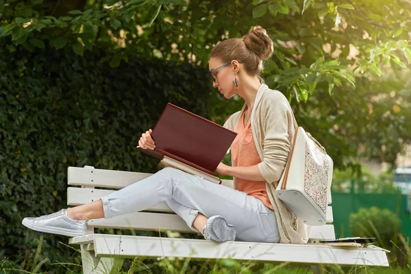 Primer plano de una chica de moda leyendo en el banco del parque — Foto de Stock