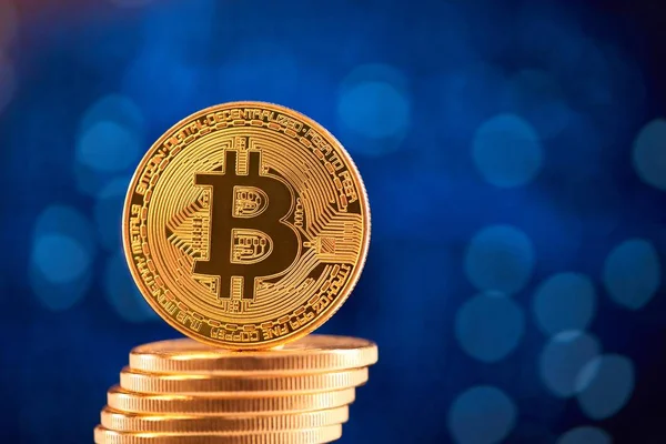 Stack av gyllene bitcoins med en bitcoin på dess kant placeras på suddig blå bakgrund. — Stockfoto