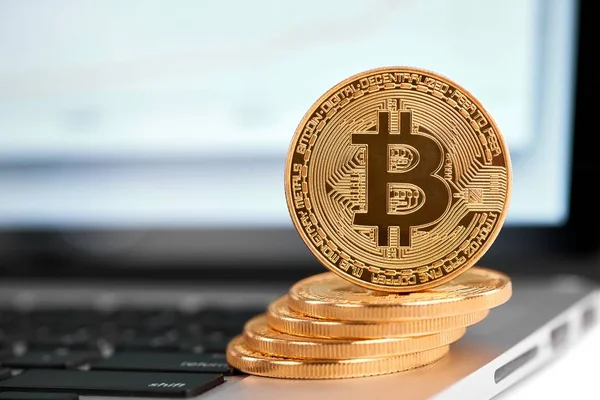 Stack of golden bitcoins with one bitcoin on its edge standing on silver laptop — Stock Photo, Image