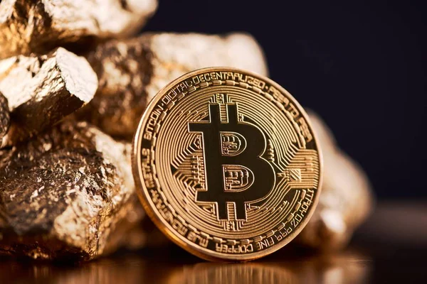 Golden bitcoin next to gold lumps representing futuristic world trends both isolated on black background — Stock Photo, Image
