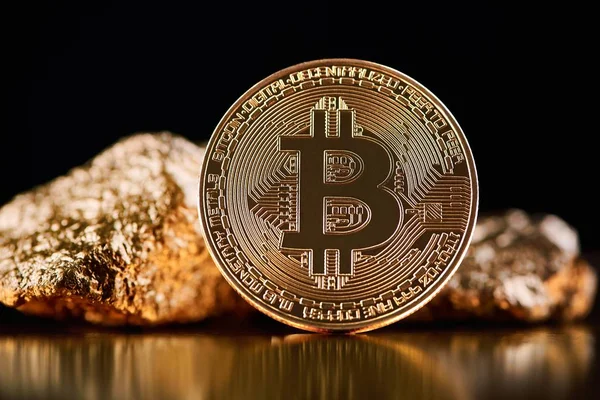 Golden bitcoin in front of gold lumps representing futuristic world trends both isolated on black background. — Stock Photo, Image