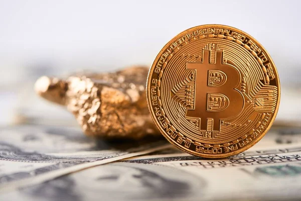 Gyllene bitcoin som viktigaste värld kryptovaluta bredvid guld klump med suddiga hundra dollar sedlar på bakgrund. — Stockfoto