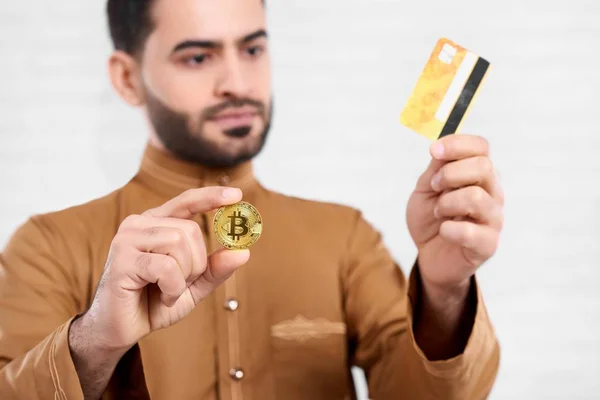 Arabian businessman keeps credit card and a golden bitcoin. — Stock Photo, Image