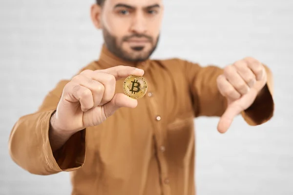Golden bitcoin hold by attractive muslim male model showing thumbs down — Stock Photo, Image