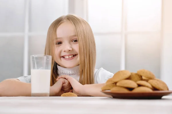 Прекрасная маленькая девочка с милой улыбкой сидит рядом с печеньем . — стоковое фото