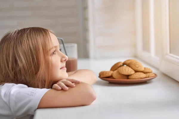 Мечтательная девушка с печеньем на подоконнике . — стоковое фото