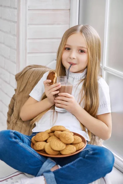 Улыбающаяся маленькая девочка пьет шоколадное молоко с печеньем . — стоковое фото