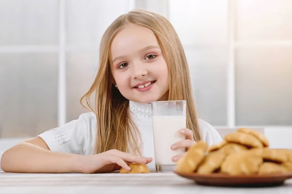 Улыбающаяся маленькая девочка сидит возле стакана молока и печенья . — стоковое фото