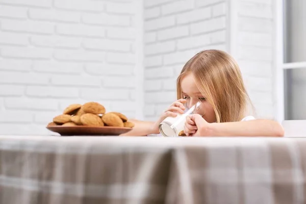 Menina bonito é beber leite perto de prato com biscoitos . — Fotografia de Stock