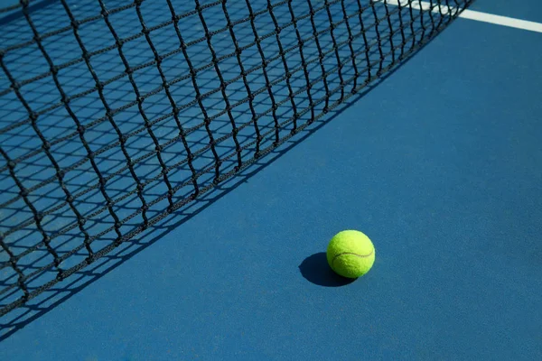 Yellow tennis ball is laying near black net.