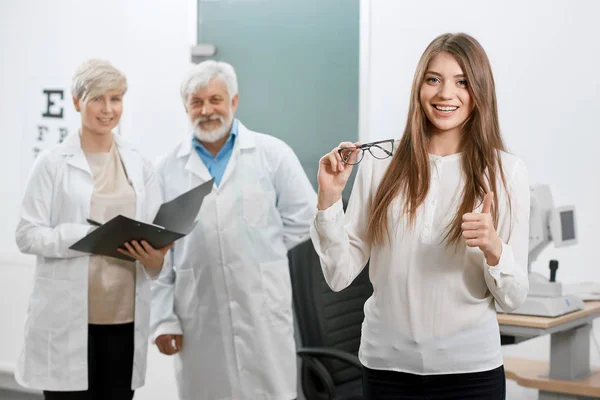 Vorderansicht eines zufriedenen Patienten, der vor dem alten Augenarzt und Assistenten lächelt. — Stockfoto